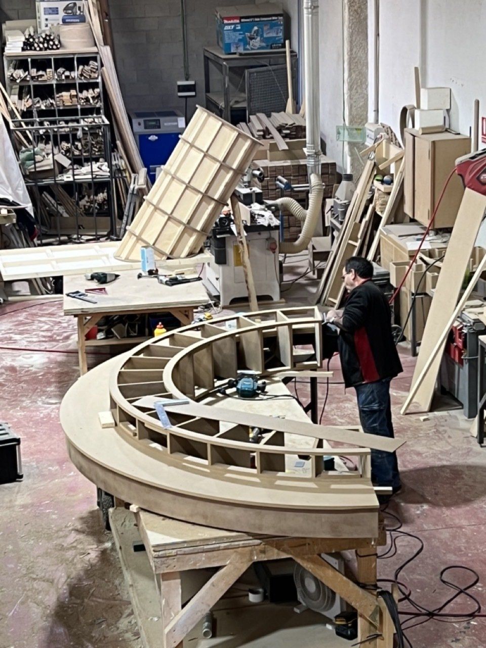 Un hombre está de pie junto a una pieza de madera curvada en un taller.