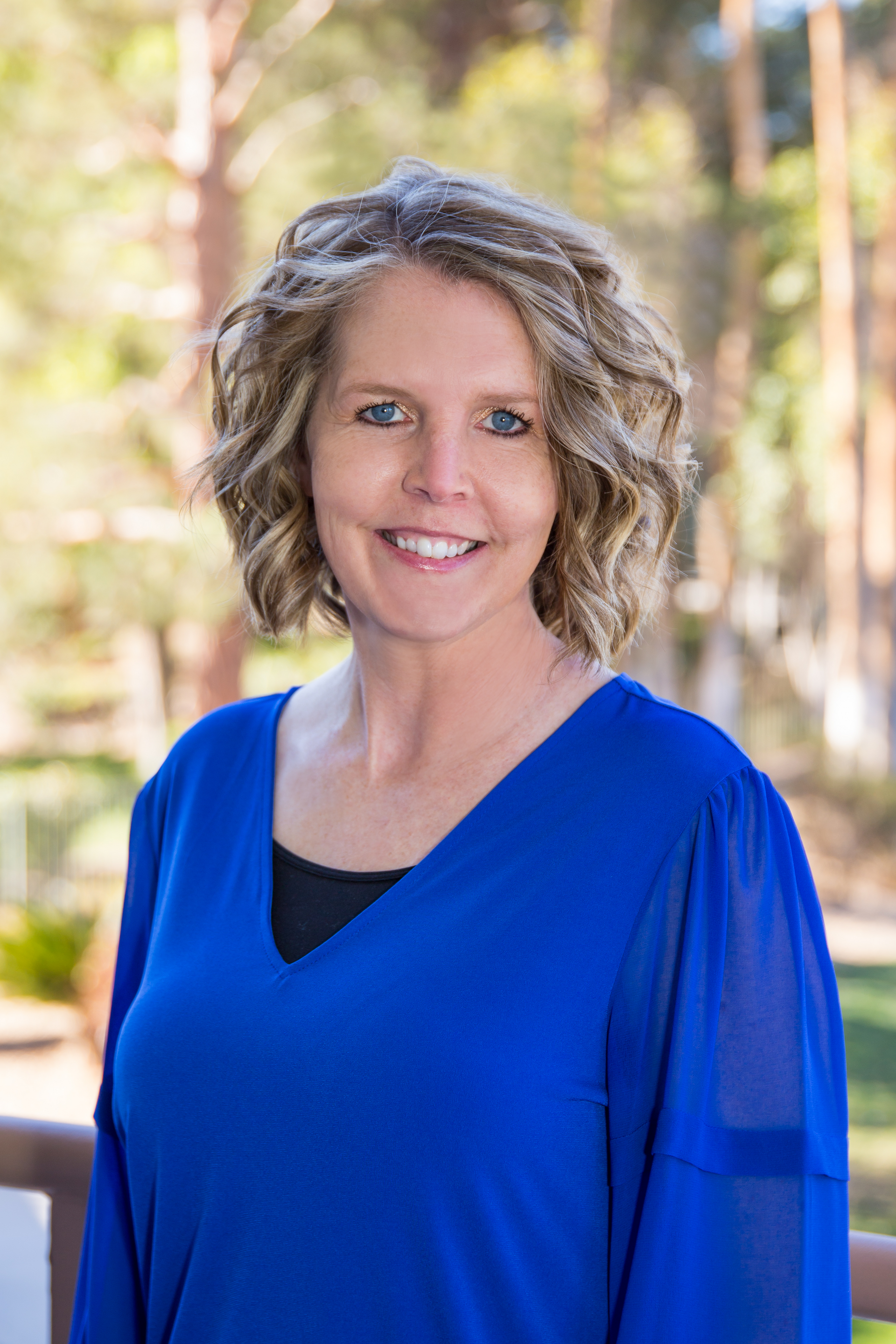 A woman in a blue shirt is smiling for the camera.