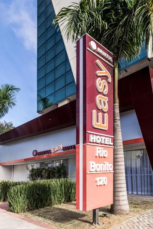 Placa do Easy Hotel Rio Bonito, vermelha e branca, ao lado do prédio do hotel.