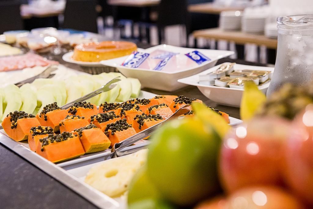 Buffet de café da manhã com mamão fatiado, melão, frutas e pratos diversos.