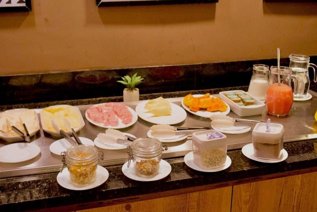Buffet de café da manhã: queijos, carnes, cereais, iogurte, sucos, leite e água.