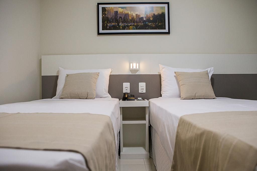 Duas camas de solteiro em um quarto de hotel com cores neutras, mesa de cabeceira e obras de arte acima.