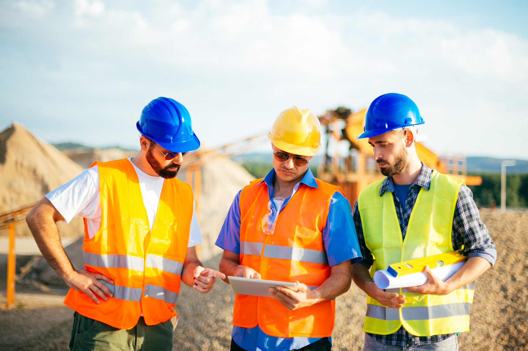 Three construction workers are looking at a tablet on a construction site.