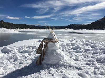 A snowman is sitting in the snow near a lake.