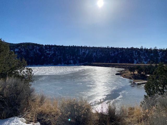 A frozen lake surrounded by snow and trees on a sunny day.