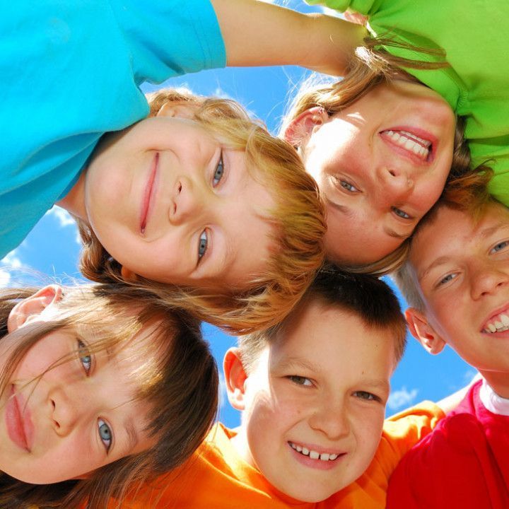 Five smiling children leaning in a circle against a blue sky.