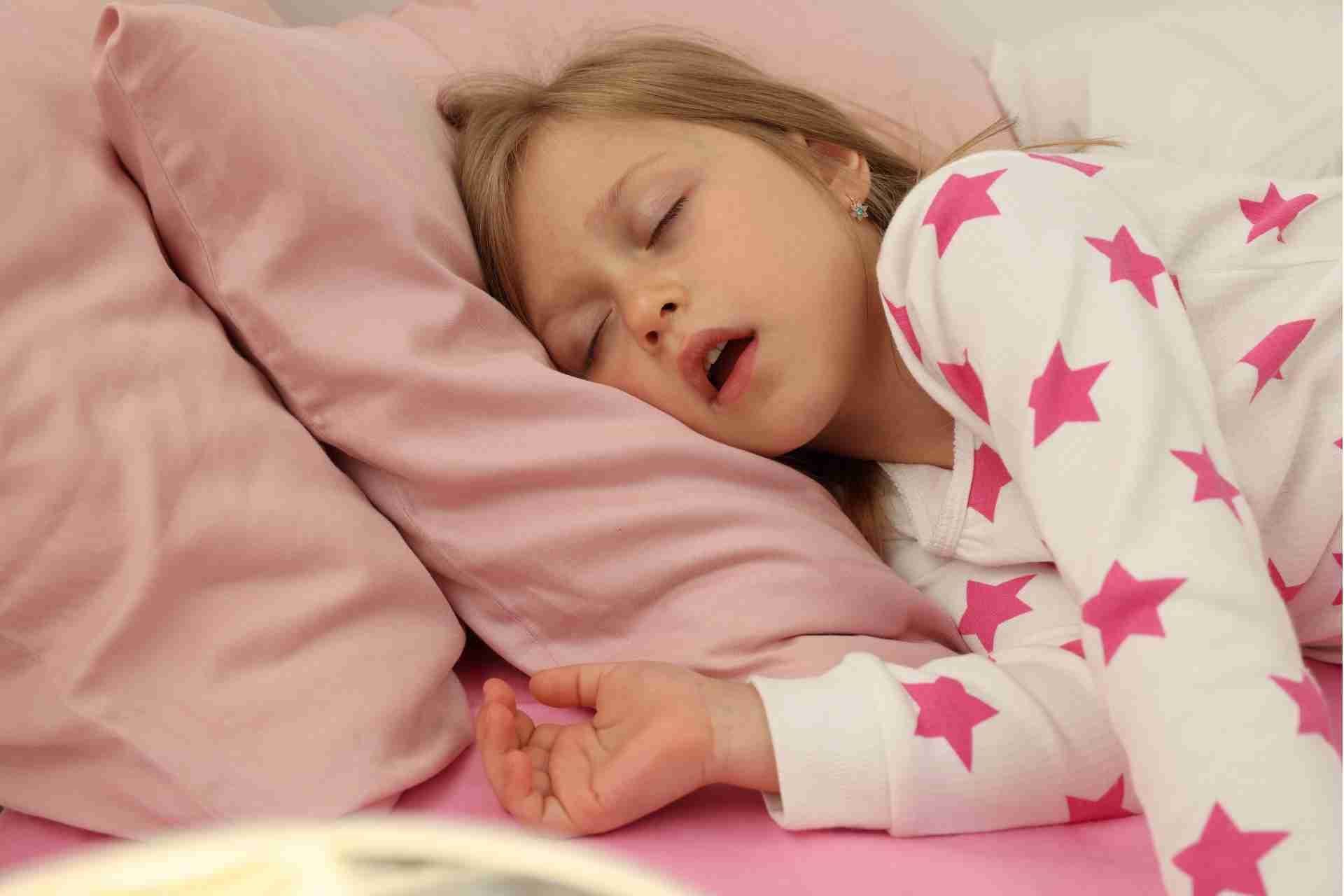Sleeping child in pink star pajamas lying on a bed with pink bedding