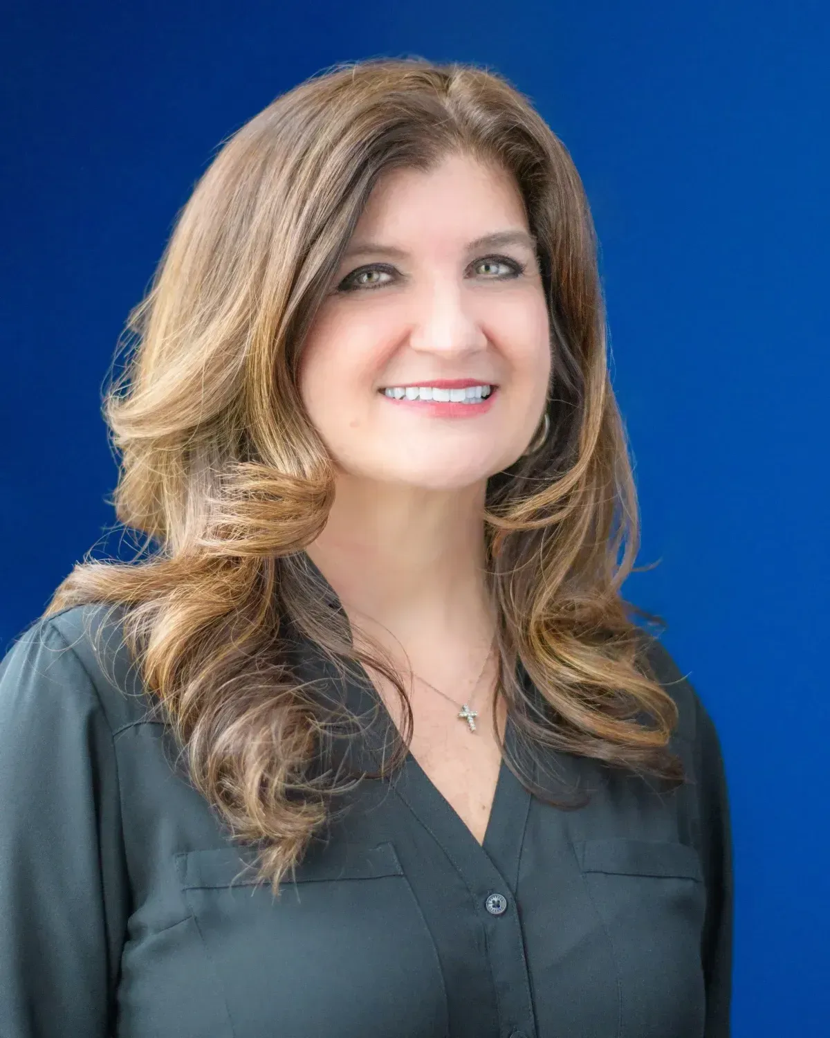 Smiling woman with long brown hair in a dark blouse against a blue background