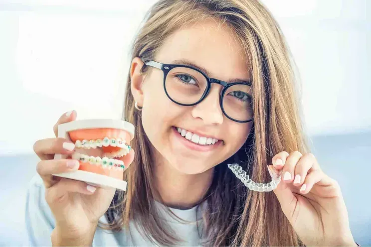 Smiling person with glasses holding a dental model and clear aligner, showing teeth straightening treatment