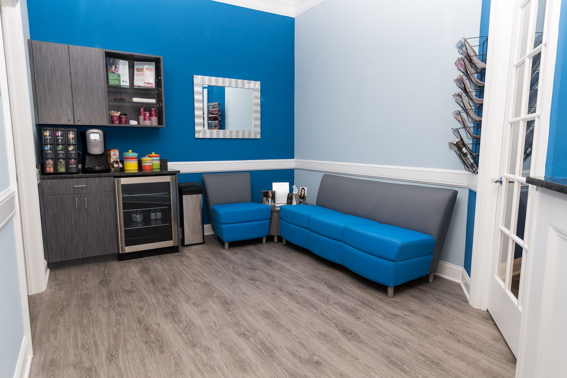 Modern lounge with blue couch, gray chair, bar cabinet, and wood flooring against blue and white walls