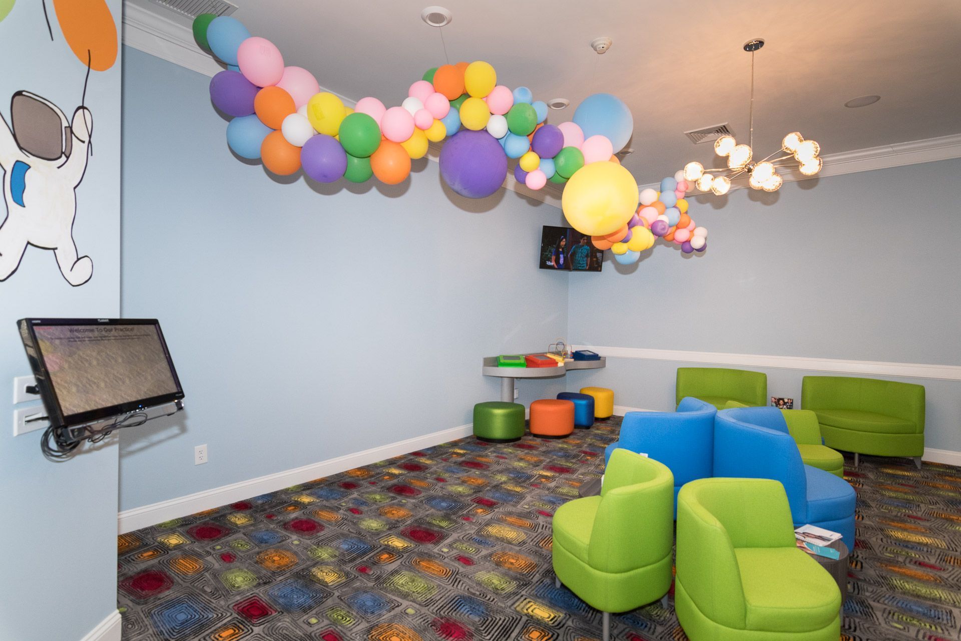 Colorful playroom with balloons, green and blue chairs, toy drums, and a patterned carpet