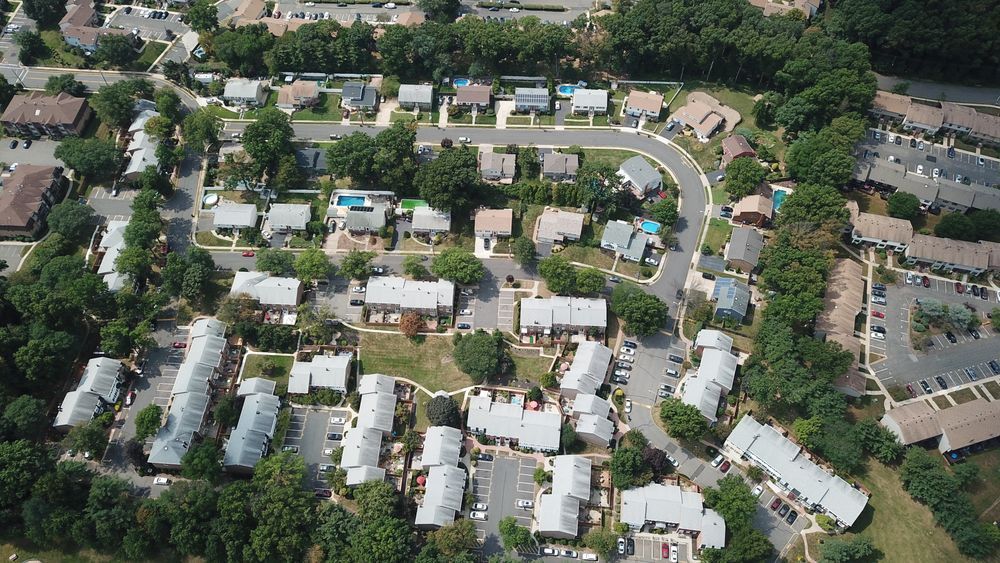 Aerial view of a tree-lined suburban neighborhood with houses, roads, and parked cars.
