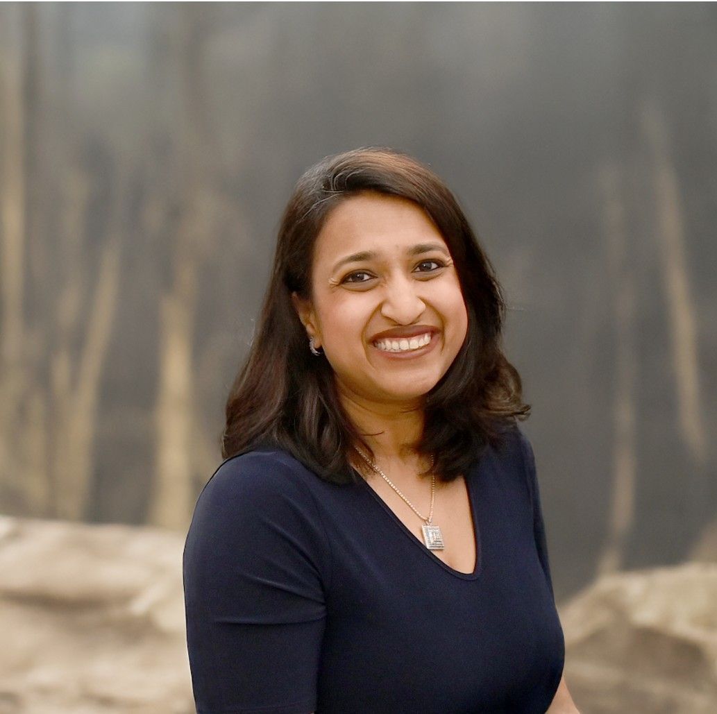 Smiling woman in a navy top standing outdoors against a blurred rocky background