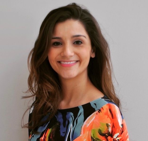 Smiling woman with long dark hair wearing a colorful floral top against a plain background