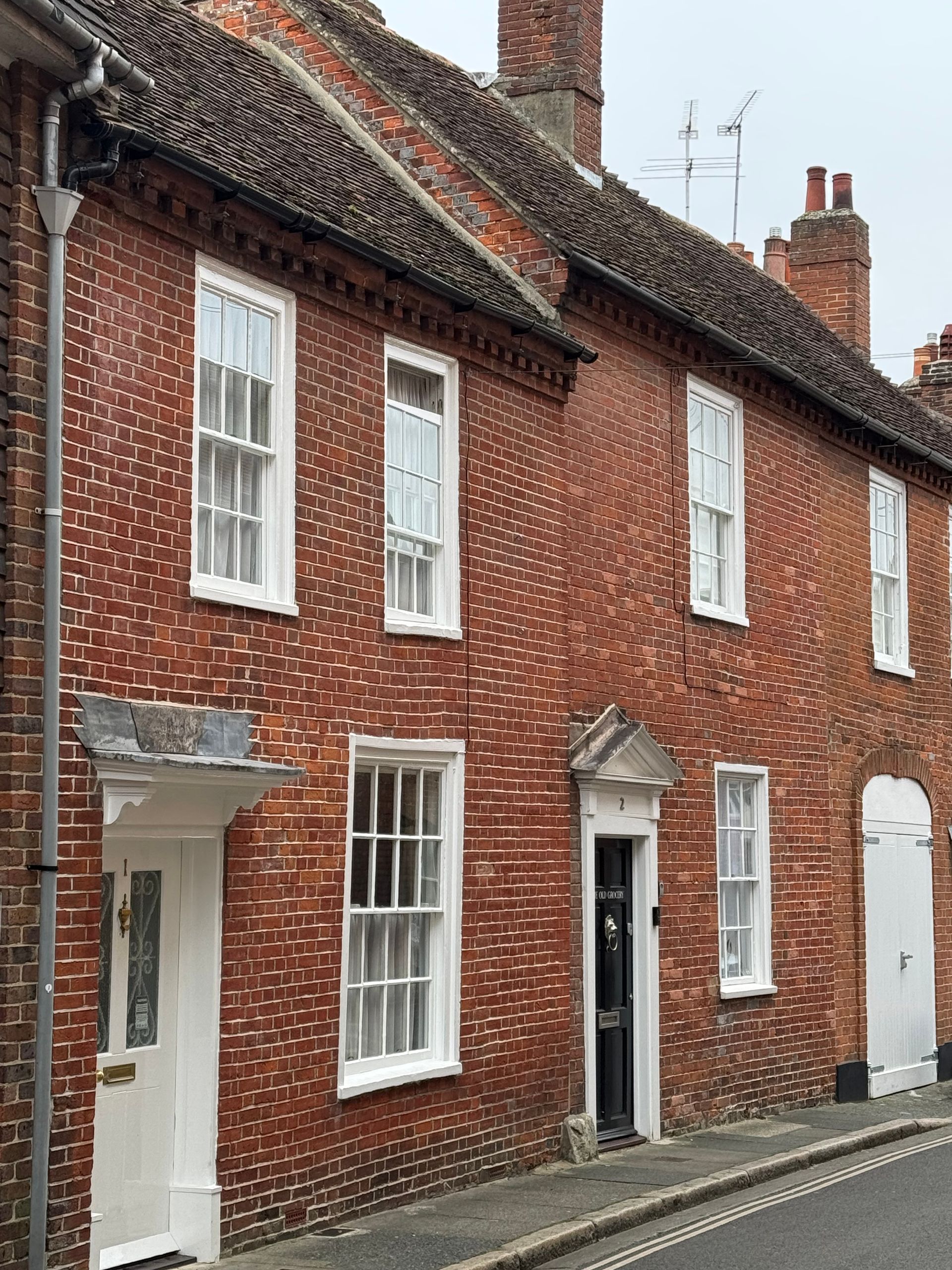 Red brick buildings with white-framed windows and doors on a street, in Chichester.