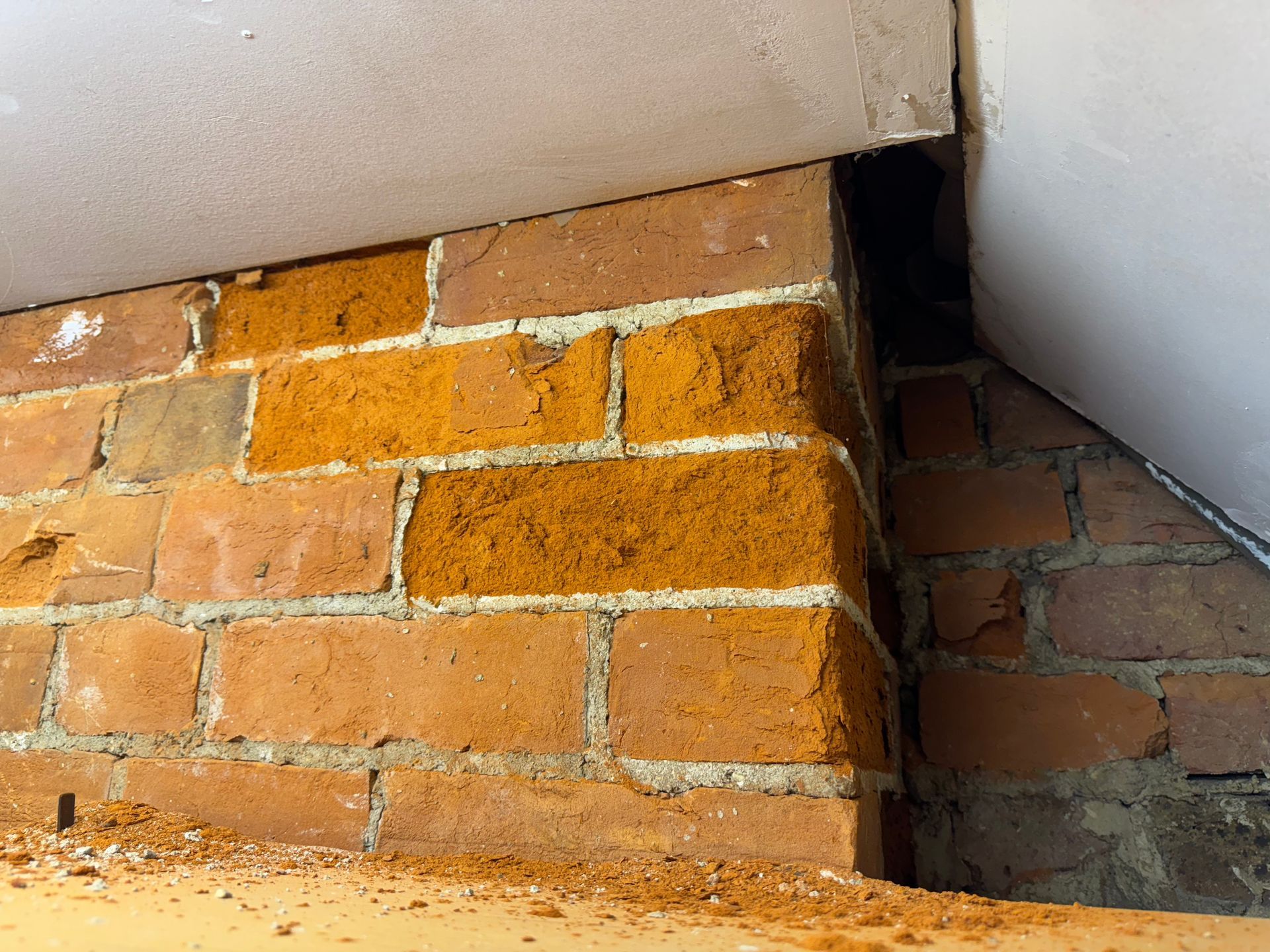 Brick wall with a dark gap in the corner under a slanted ceiling.  Bricks are spalling.