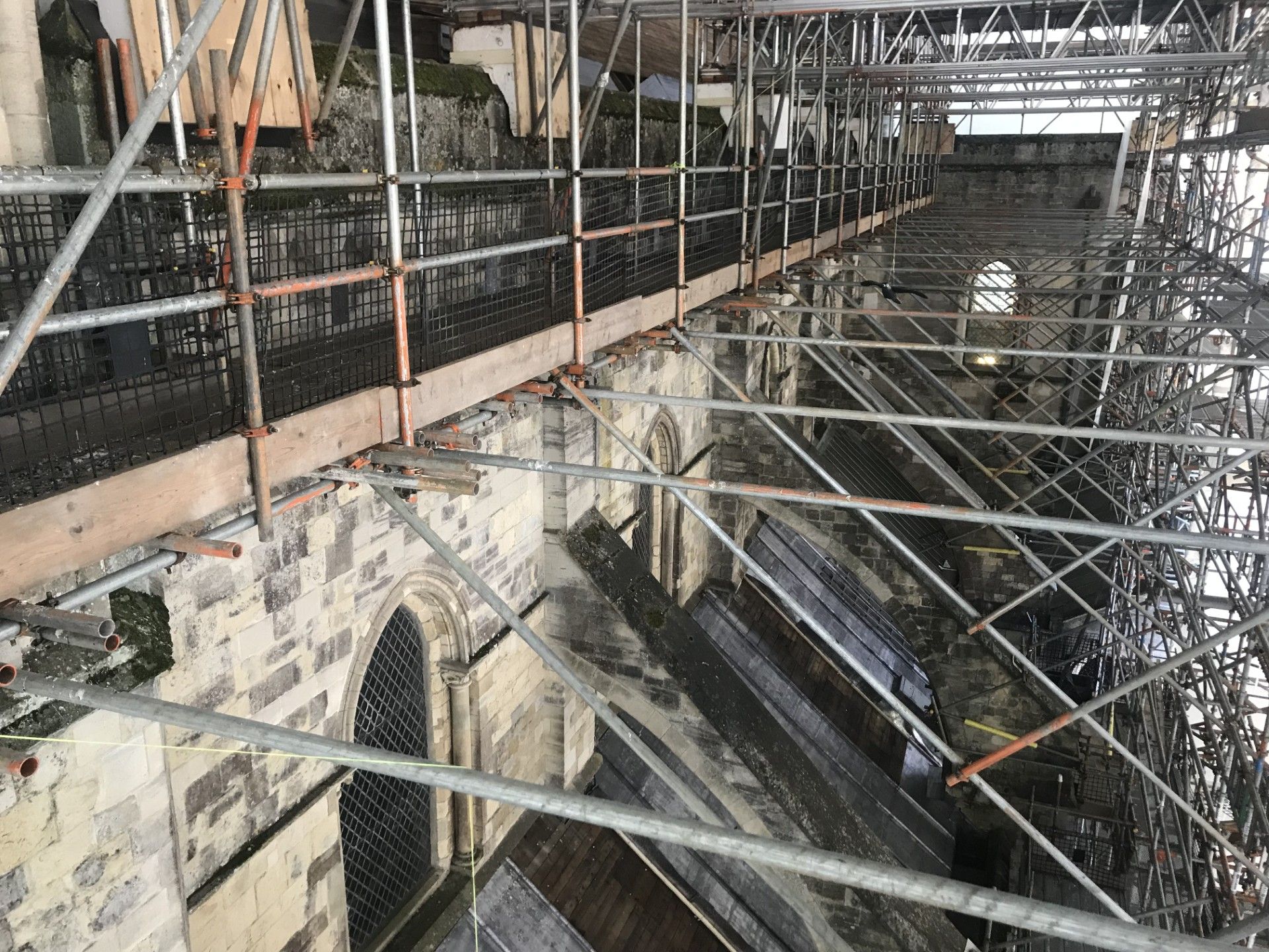 Scaffolding surrounds a church interior under renovation, with stone arches and metal beams visible.