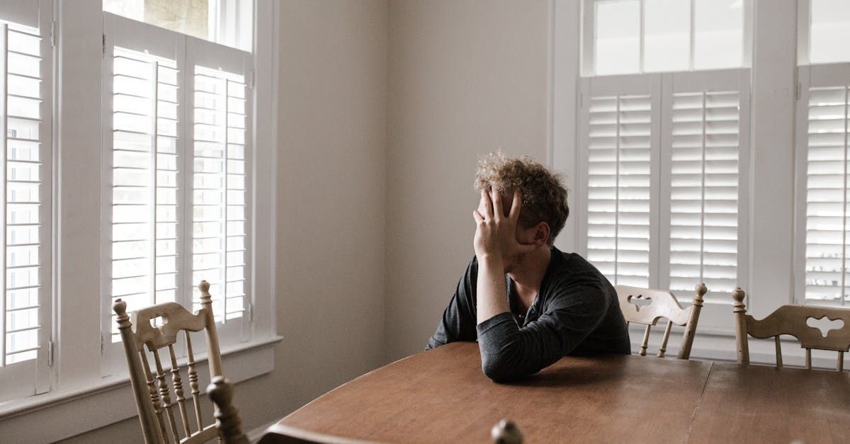 A person is sat at the kitchen table with his head in his hand looking concerned