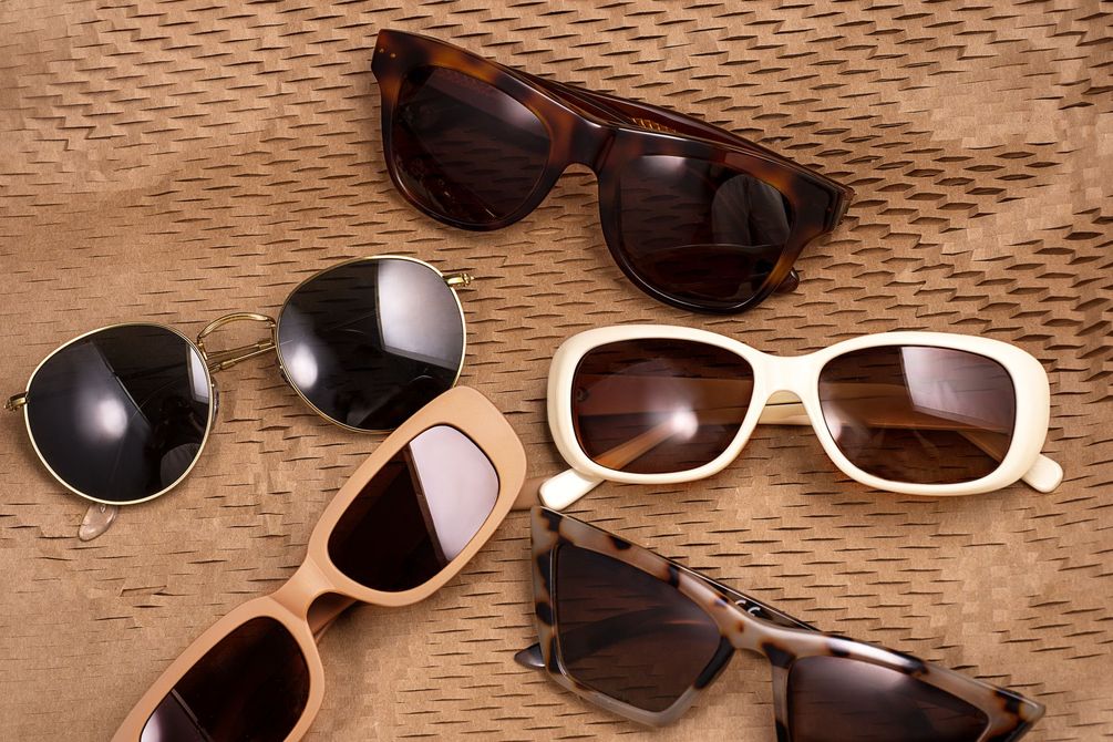 Occhiali da sole assortiti con montatura marrone, bianca e nera su una superficie intrecciata color cuoio.