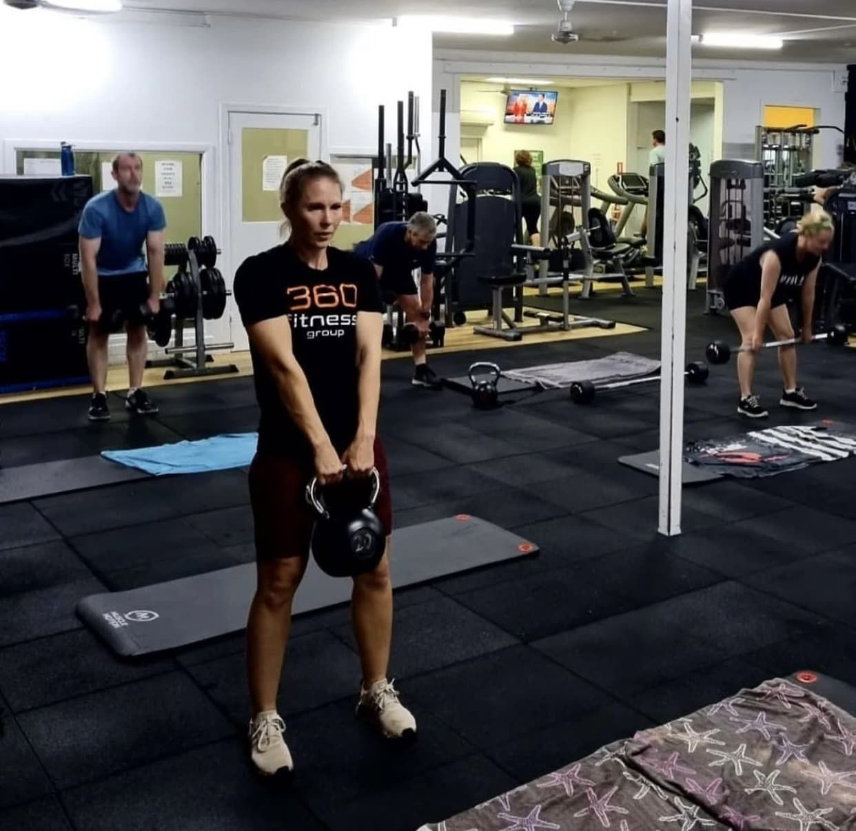 A Woman In A 360 T-shirt Is Holding A Kettlebell In A Gym — 360 Fitness Group in Gordonvale, QLD