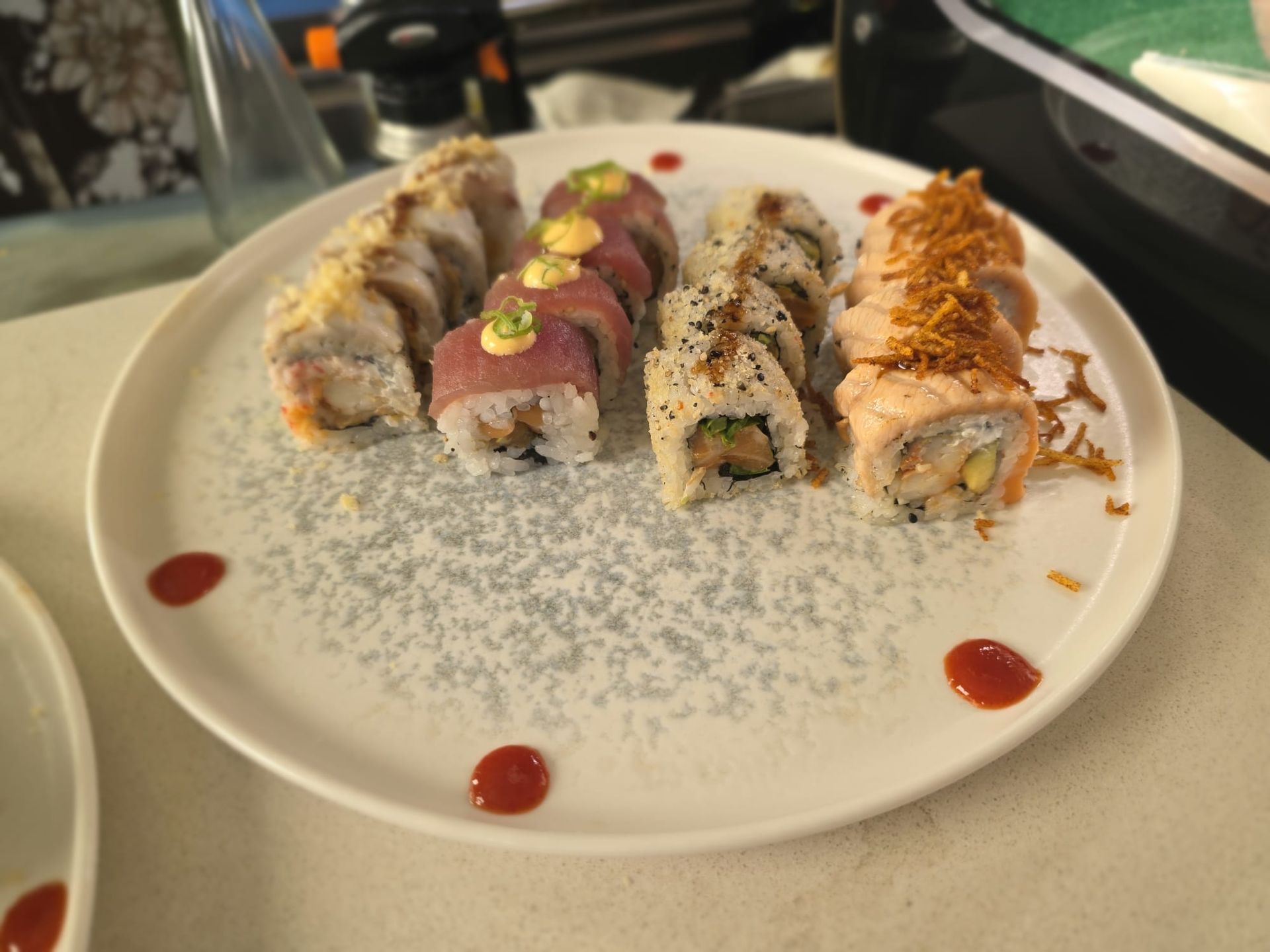 Assortimento di sushi roll su un piatto bianco, con salsa rossa a filo e semi di sesamo