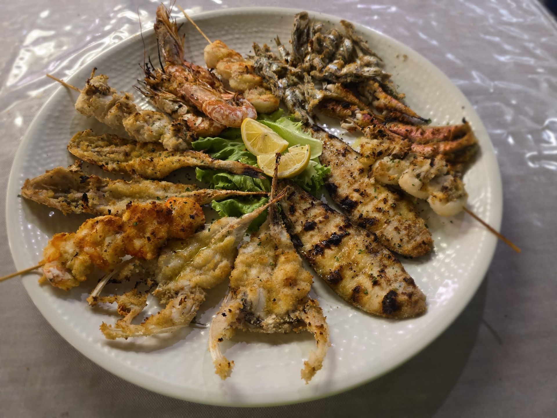 Piatto di spiedini misti alla griglia con spicchi di limone su una tovaglia bianca