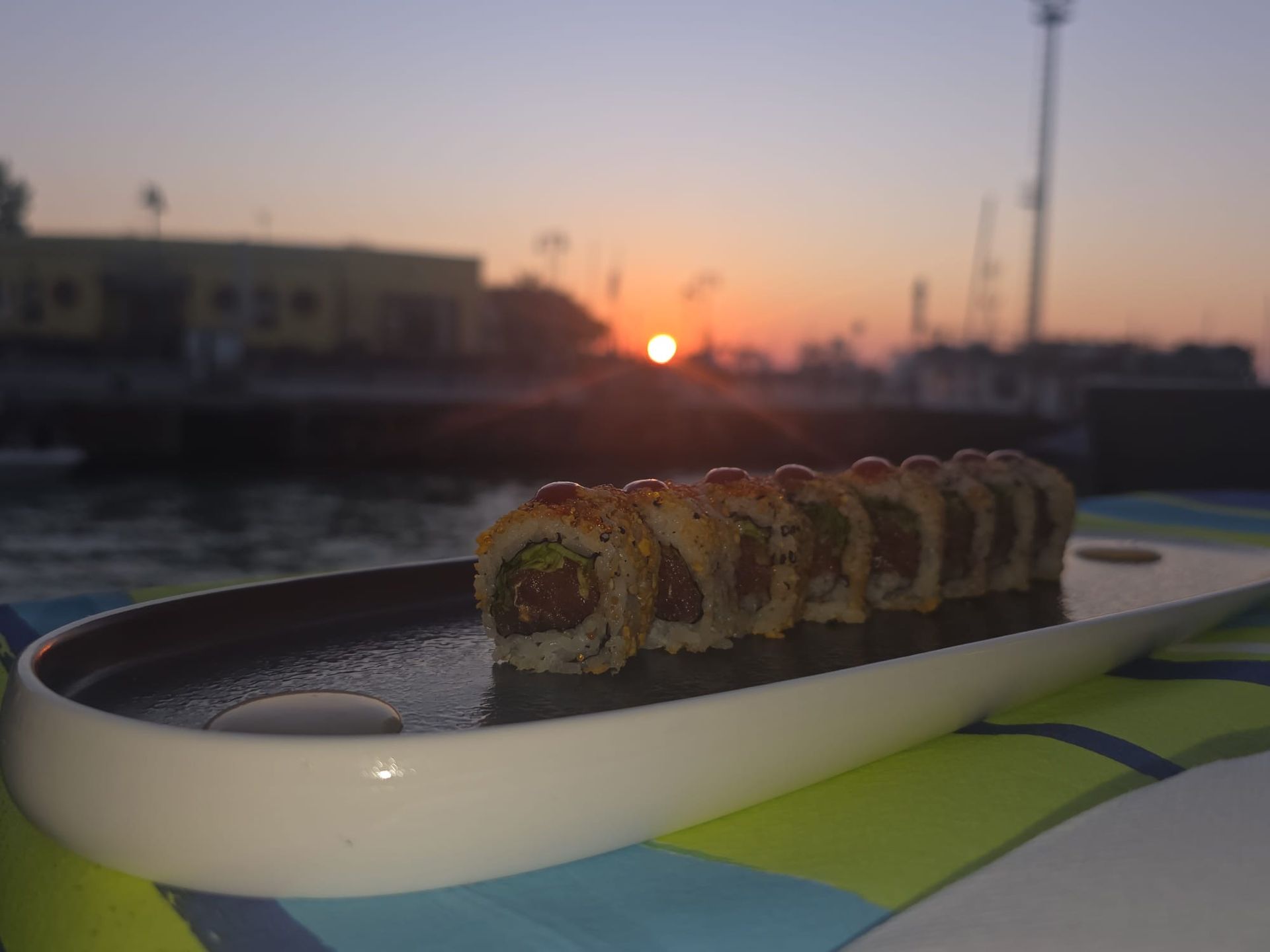 Roll di sushi su un vassoio bianco al tramonto, in riva all’acqua, con lo skyline della città sullo sfondo