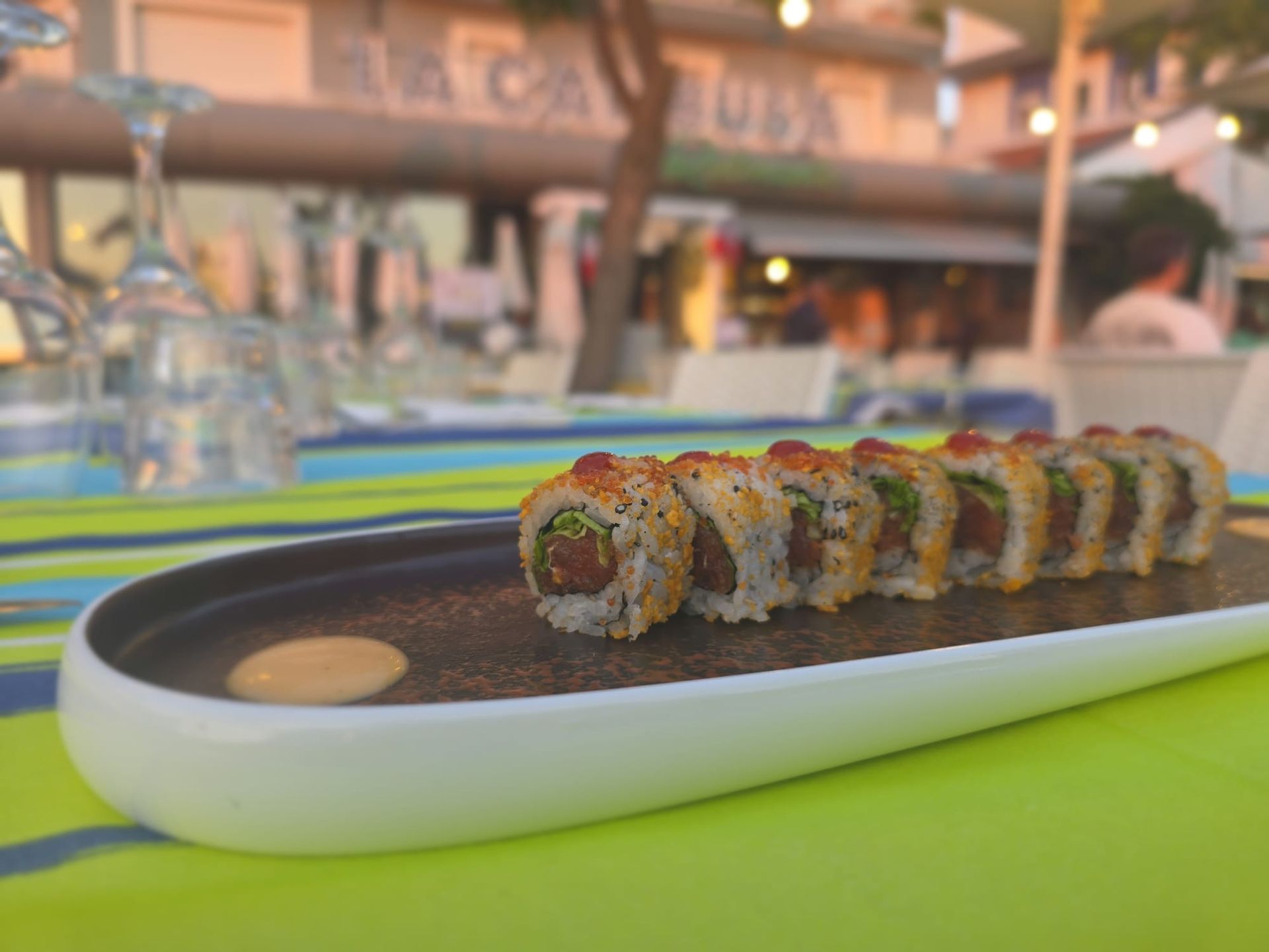 Rotolo di sushi su un piatto nero con salsa, appoggiato sul bancone di un ristorante