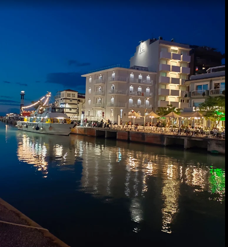 Porto al tramonto, con gli edifici illuminati sul lungomare e le barche riflesse sull’acqua calma