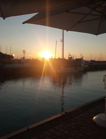 Tramonto su un porto tranquillo, con barche e ombrelloni stagliati contro il cielo arancione.