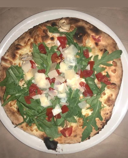 Piatto bianco con una pizza bruciacchiata guarnita con rucola, peperoni rossi e formaggio fuso