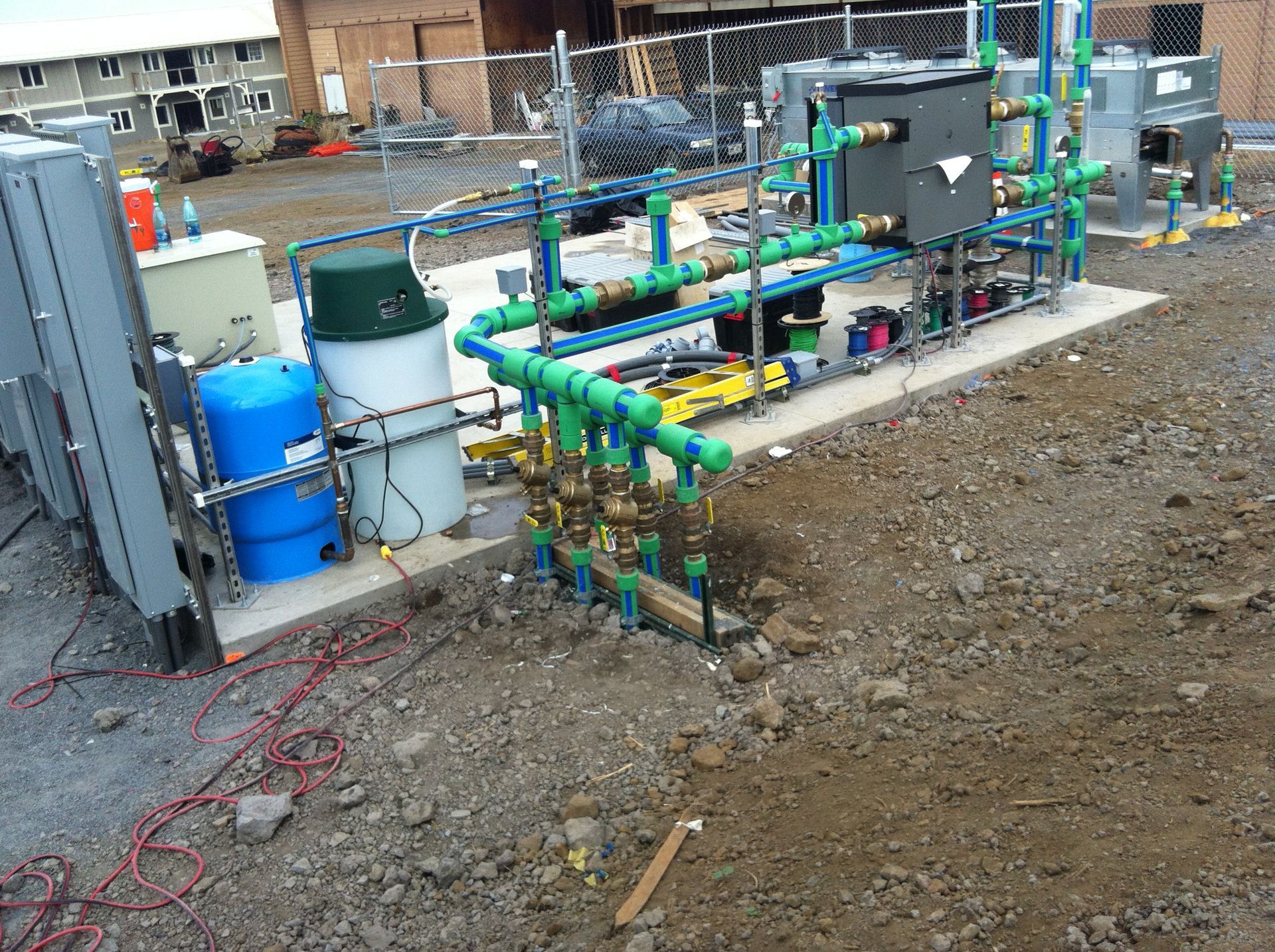 Outdoor industrial piping system with green and blue pipes, tanks, and machinery on a dirt construction site