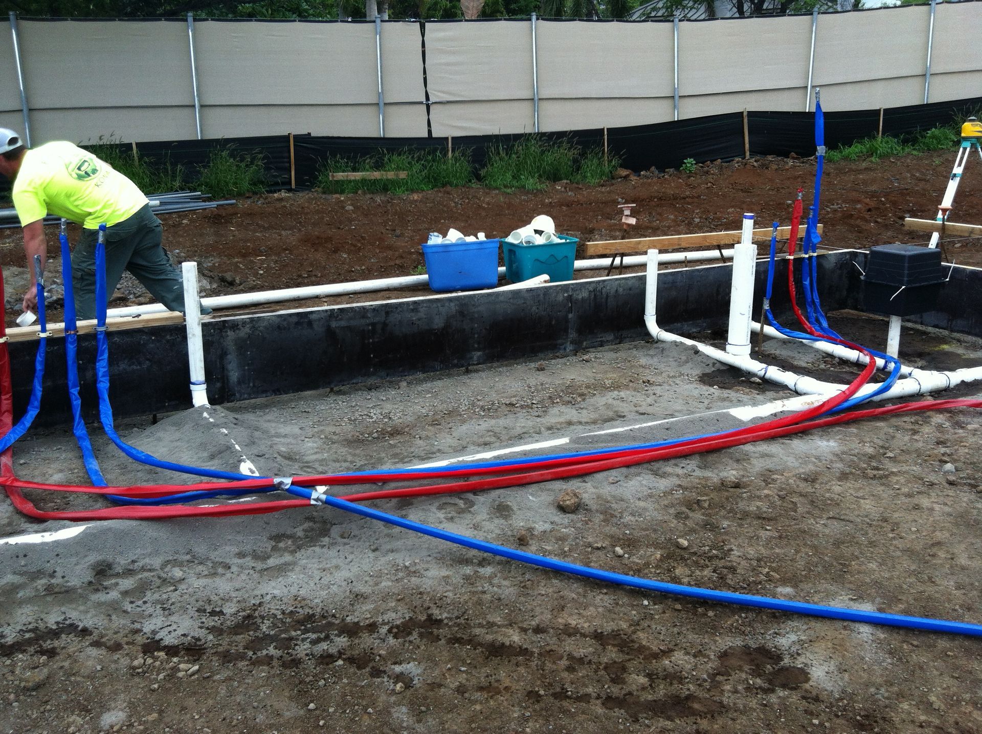 Worker installing blue and red pipes at a construction site with a concrete trench in the foreground