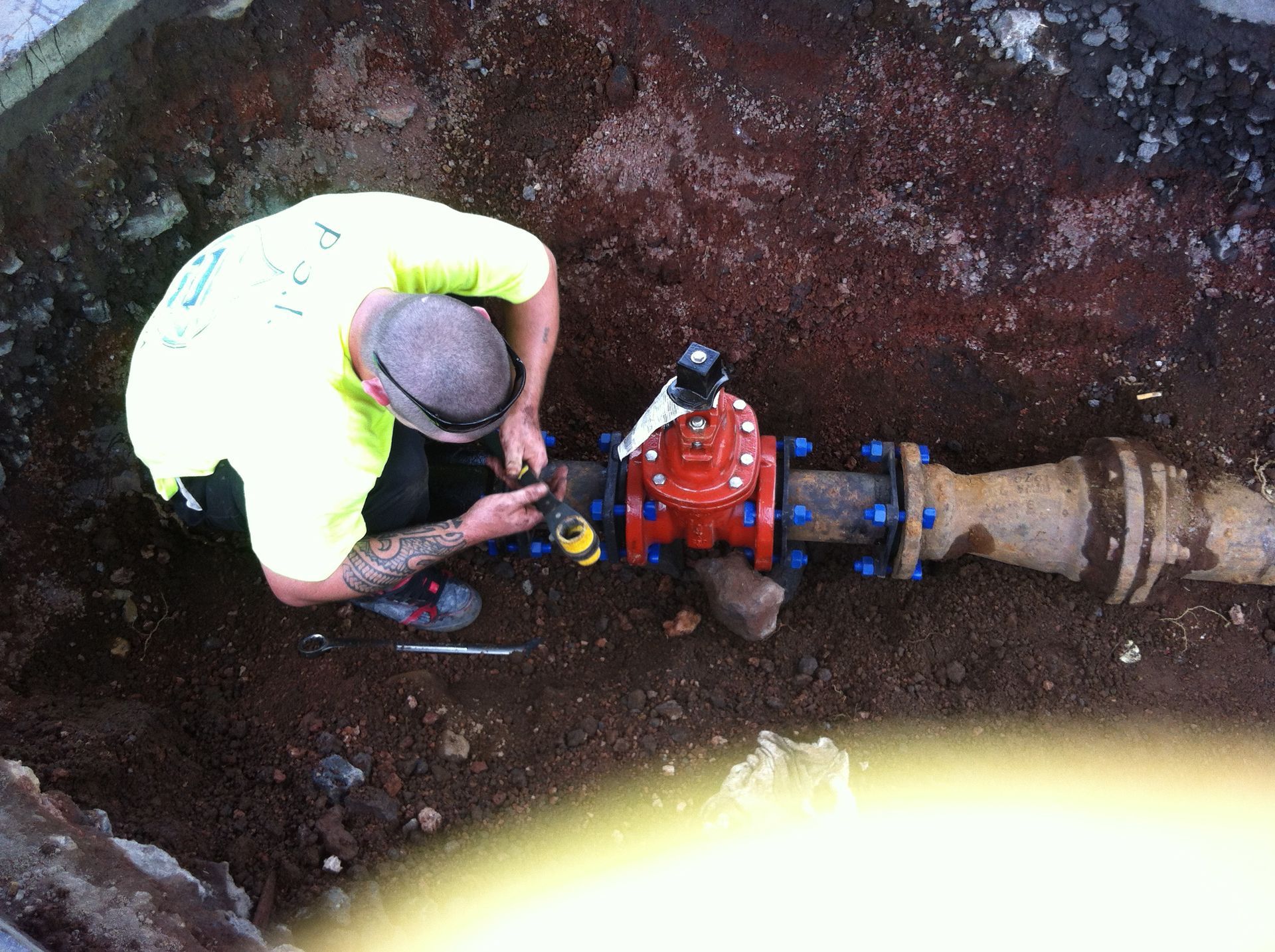 Worker in a trench inspecting a red underground valve on a blue pipe system