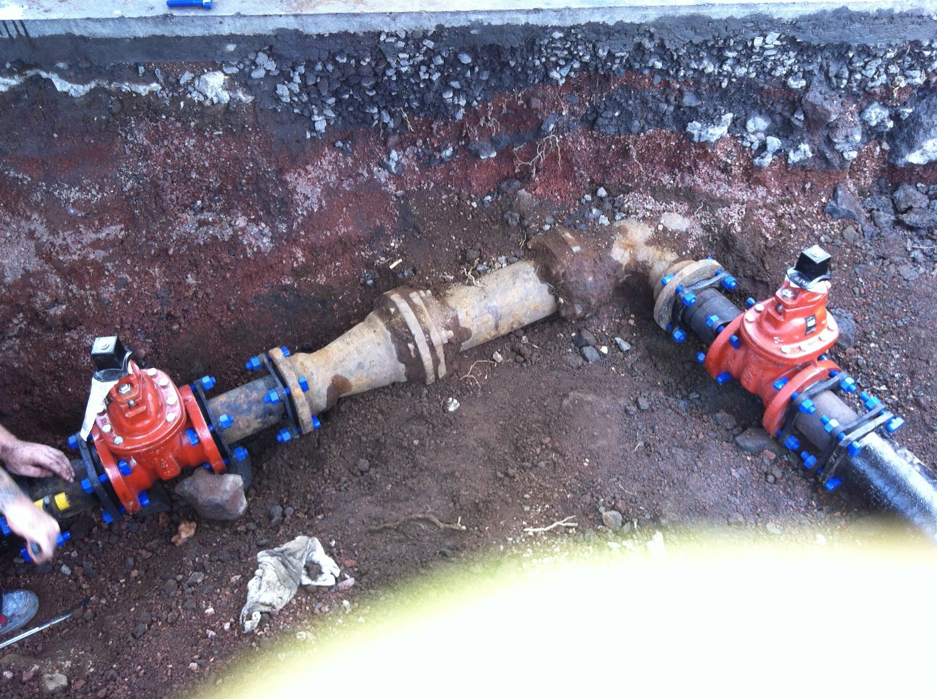 Two red valves on a blue underground pipe with a central coupling in a trench
