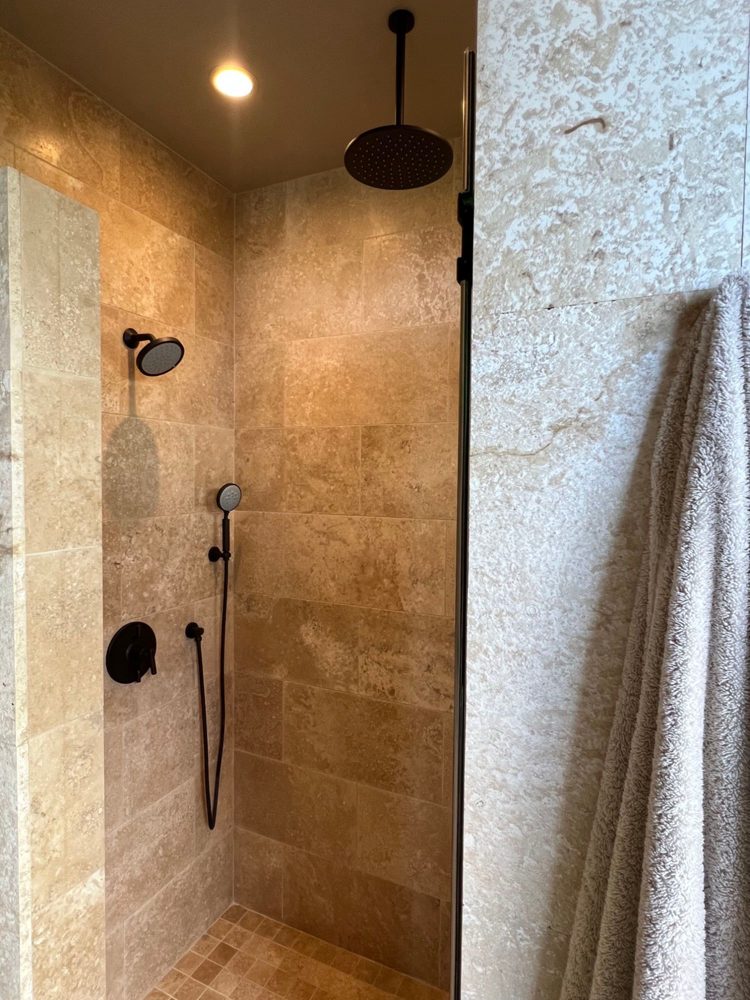 Walk-in shower with beige tile walls, black fixtures, and a towel hanging on the side