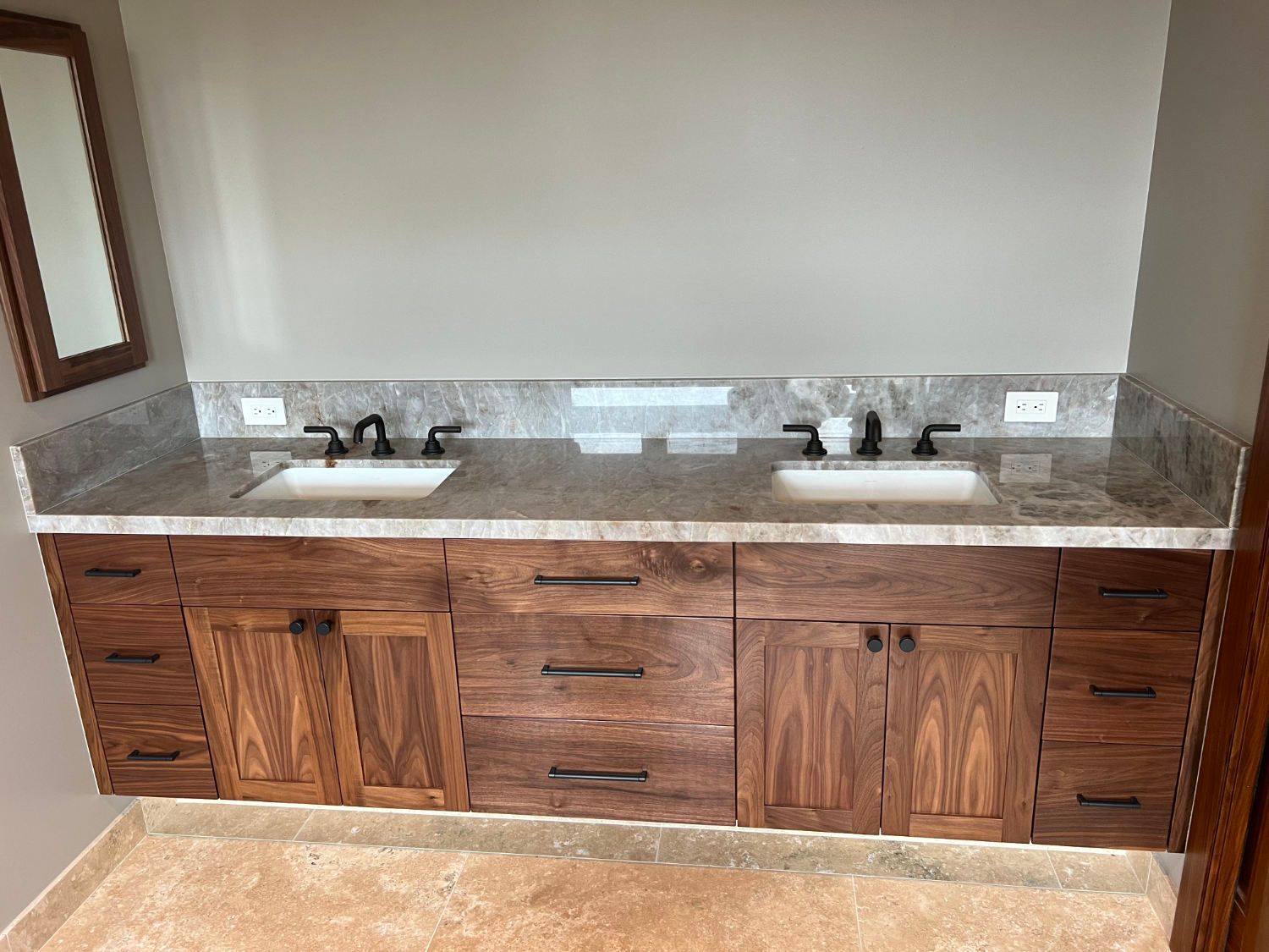 Bathroom vanity with double sinks, granite countertop, and wooden cabinets against a beige wall