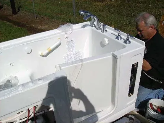 Man installing a white walk-in bathtub outdoors, holding a tool.