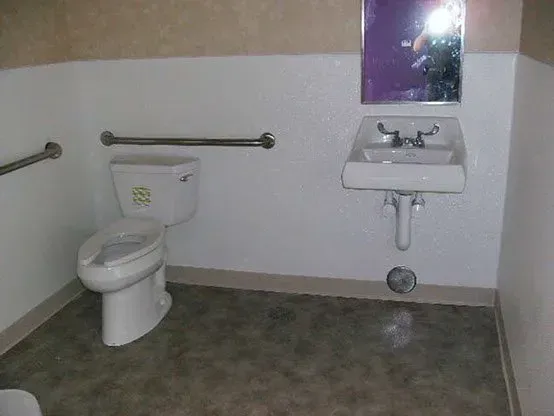 Accessible public restroom with toilet, sink, mirror, and grab bars.