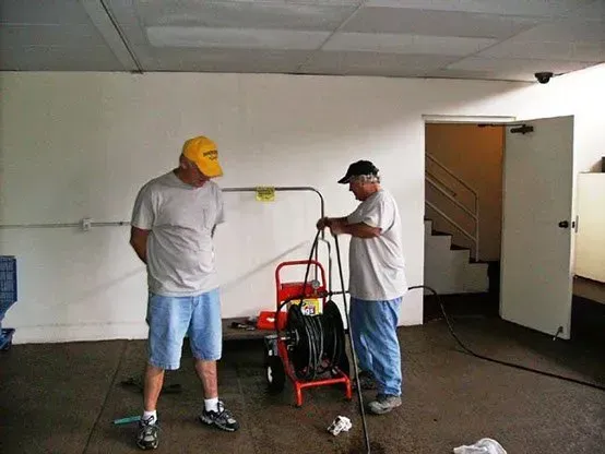 Two men prepare a sewer jetter in a utility room. 