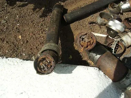 Rusty metal pipes and rings lying on the ground next to a white surface, in an outdoor setting.