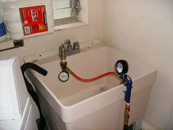 A utility sink with a pressure gauge and spray gun hooked up, testing something.