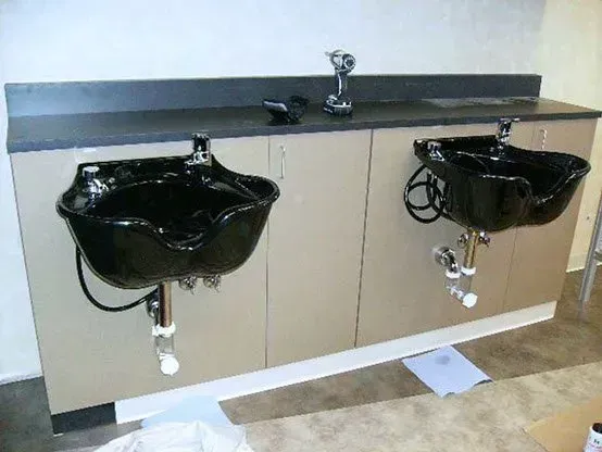 Two black shampoo bowls installed on a beige cabinet in a salon.