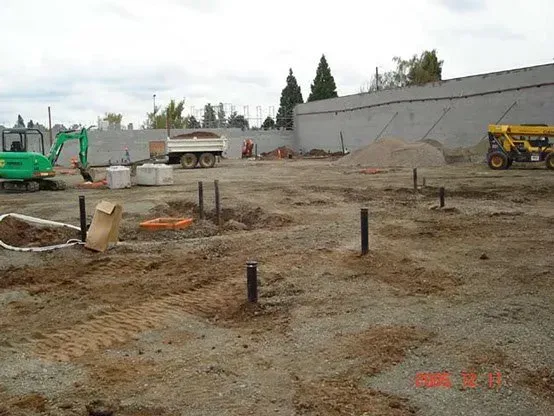 Construction site with earth-moving equipment, dirt, and foundation footings.