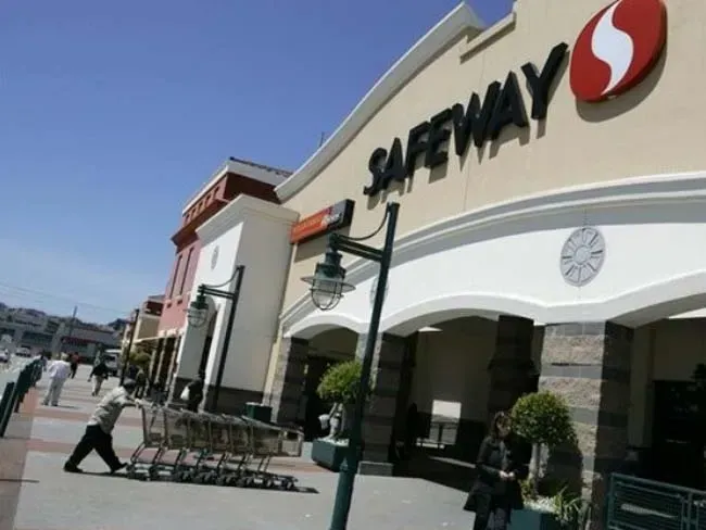 Safeway store exterior with sign, people, shopping carts on a sunny day.