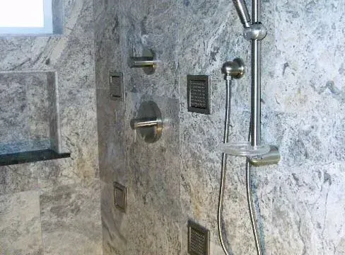 Gray marble shower with silver fixtures, including a handheld showerhead, soap dish, and water controls.