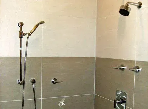 Shower stall with gray and beige tile, chrome fixtures, and hand shower.