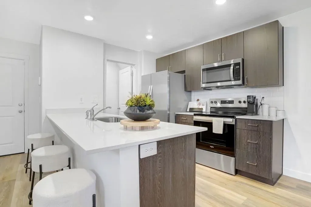 Modern apartment kitchen with white quartz countertops, dark wood cabinets, stainless steel appliances, and a breakfast bar with stools at Little Valley, offering apartments for rent in Magna, UT.