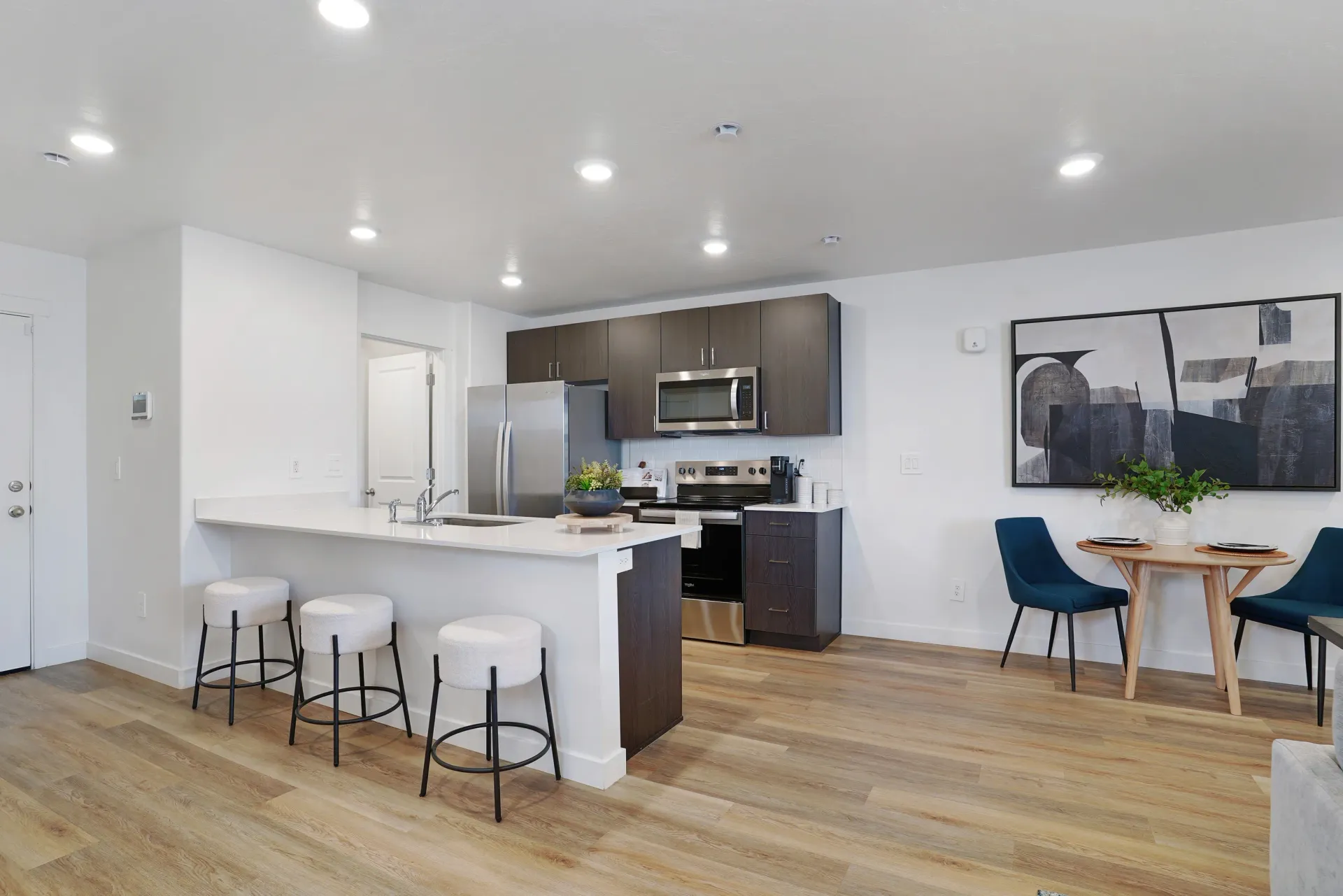 Modern kitchen and dining area with stainless steel appliances, white island with stools, and blue chairs at a round table at Little Valley, offering apartments for rent in Magna, UT.
