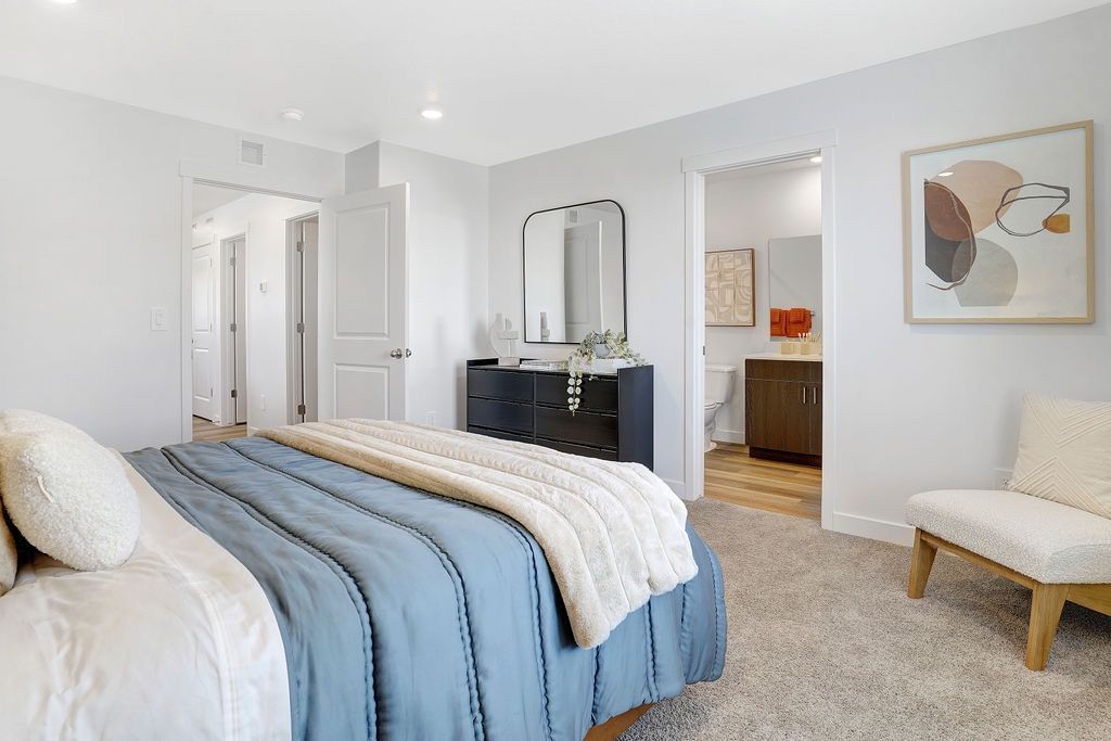 Bedroom in a modern apartment with a blue bedspread, dresser, and doorway to a bathroom.